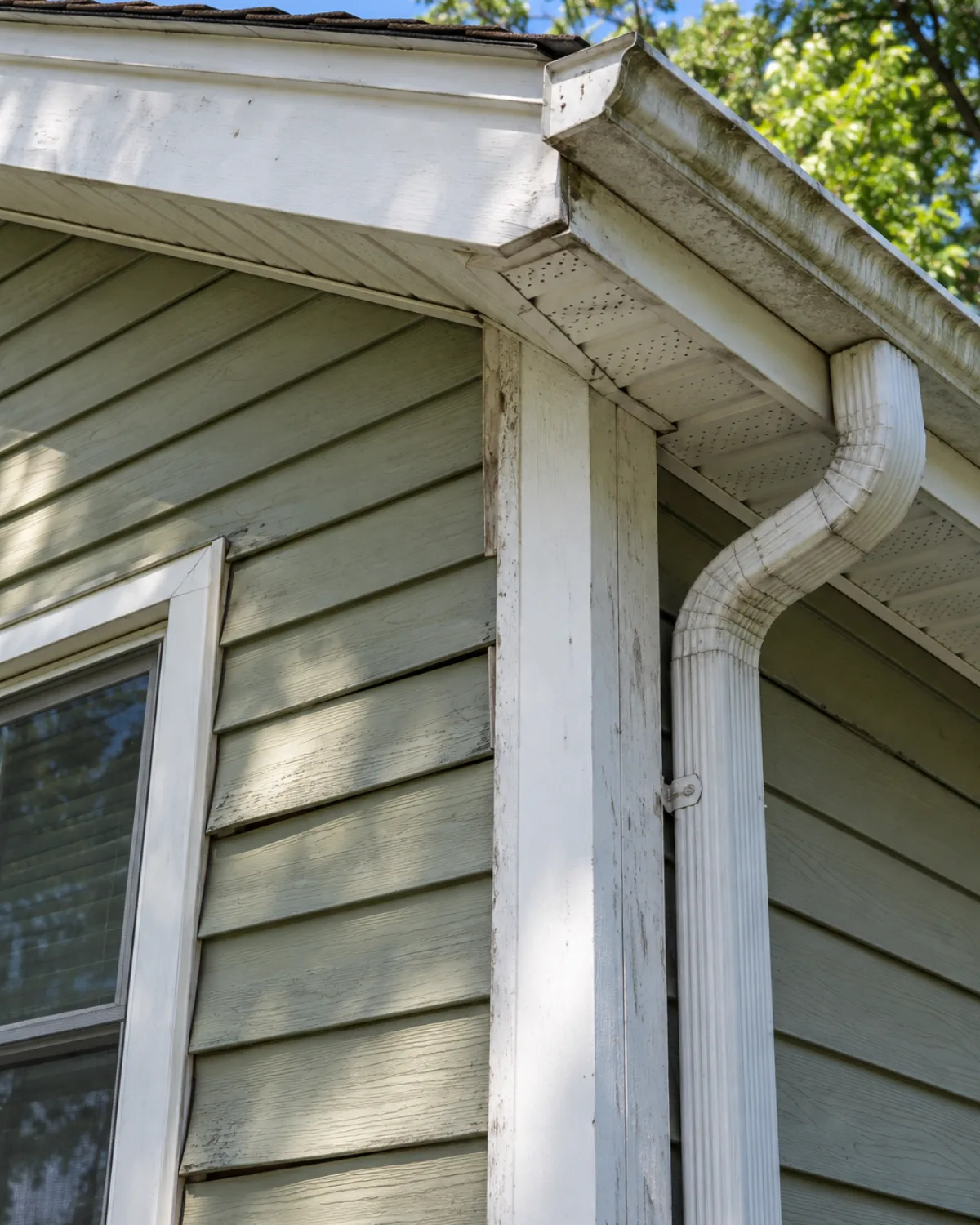 Weathered corner post and trim on lap siding, with staining along the gutter and soffit