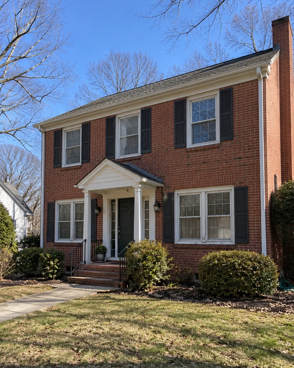 Brick colonial home with white-trimmed double-hung windows, black shutters and a covered entry door