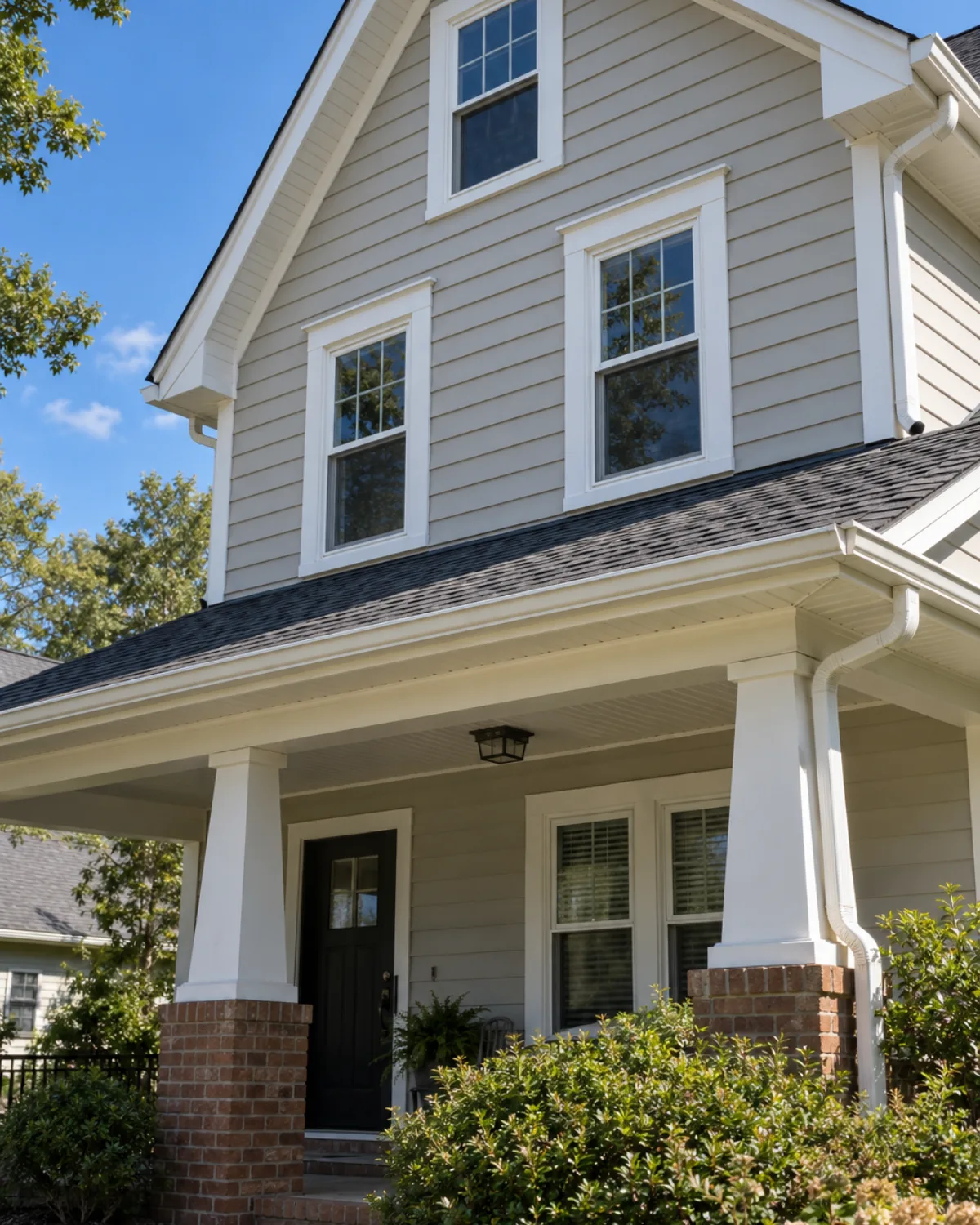 Cream lap siding home with white-trimmed double-hung windows and a dark entry door under a covered porch